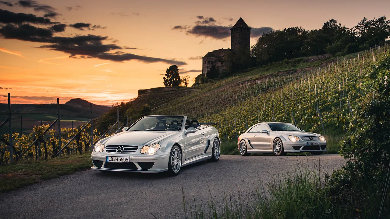 Zwei silberne Mercedes-Benz Klassiker auf einer Straße vor einer Burg und Weinbergen der Region Ludwigsburg im Abendlicht.