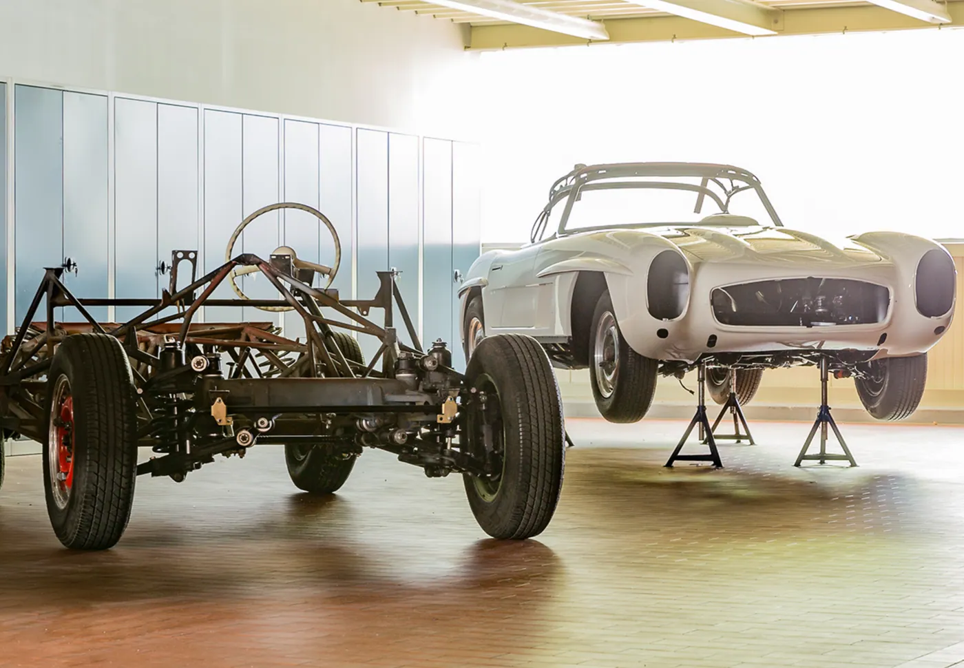 Klassiker-Restaurierung in heller Werkstatt: eine Mercedes-Benz 300 SL Karosserie neben einem Fahrgestell.